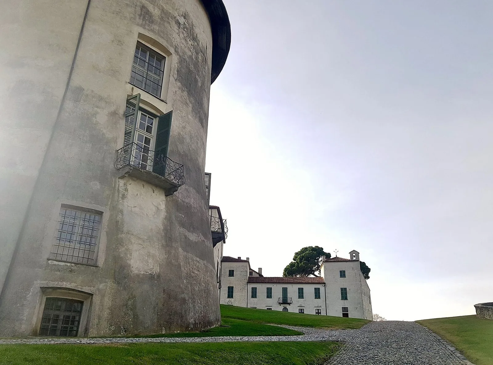 Torre circolare e facciate bianche del Castello di Masino a Caravino, con viale acciottolato e prato