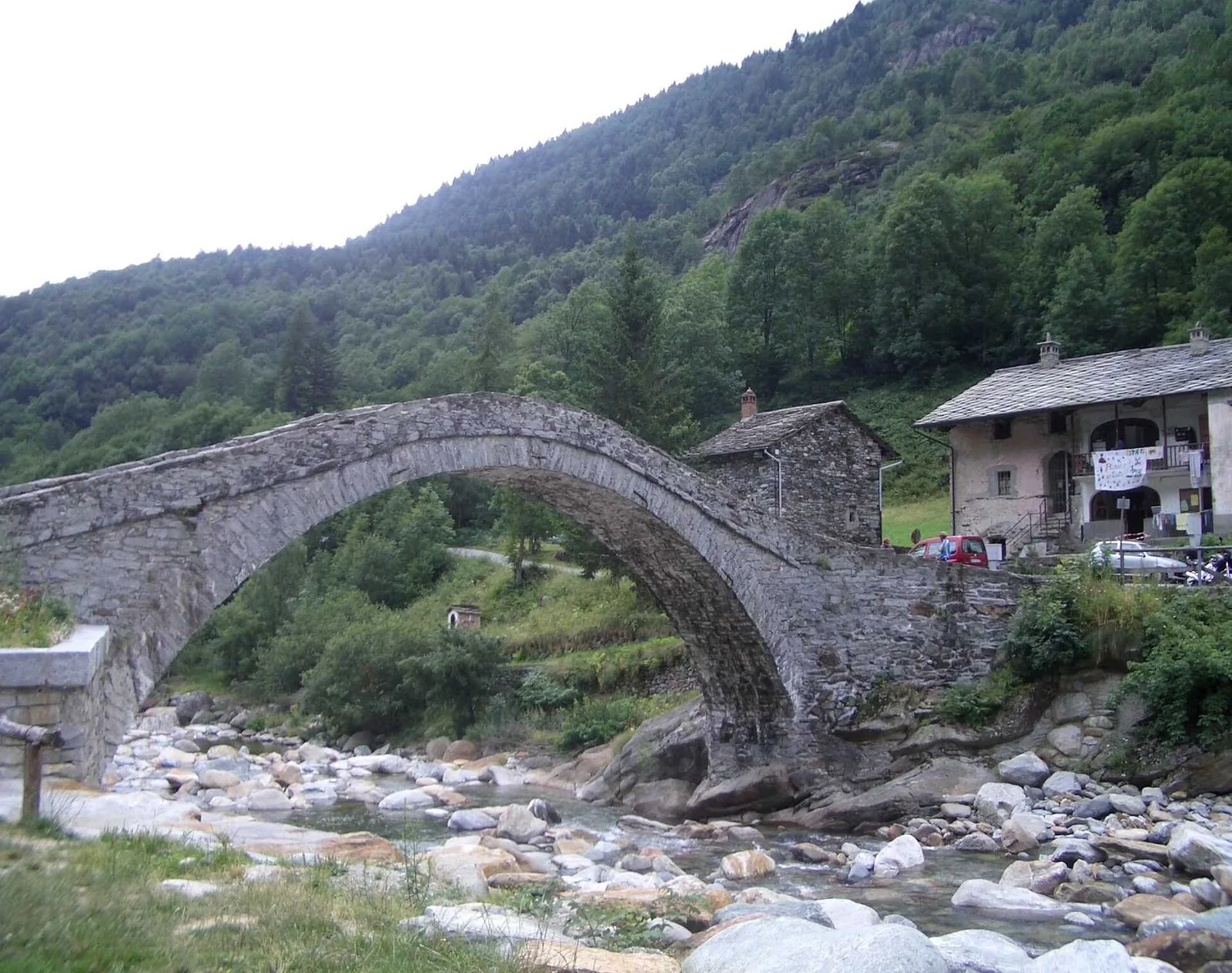 Ponte in pietra a schiena d'asino sul torrente a Fondo di Traversella, in Valchiusella, con case in pietra e boschi